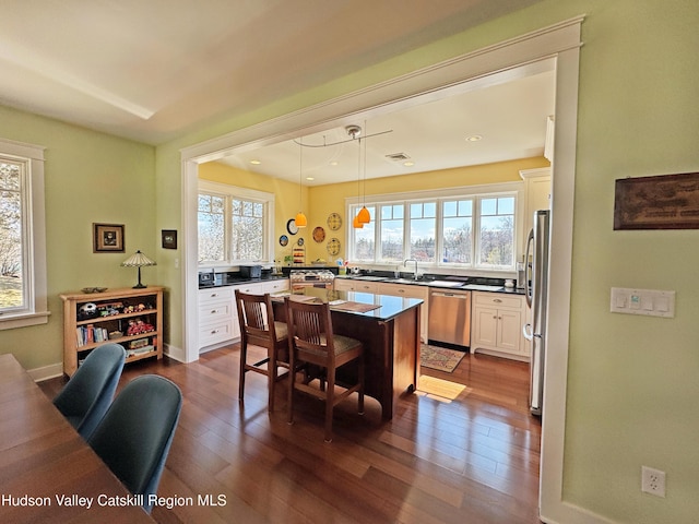 kitchen featuring dark wood finished floors, a kitchen island, stainless steel appliances, a kitchen bar, and white cabinetry