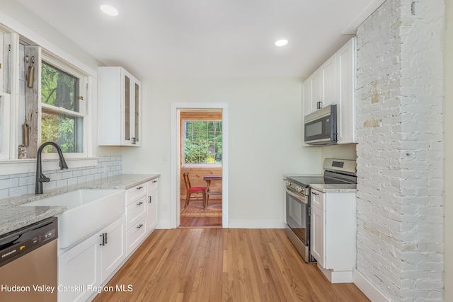 kitchen with glass insert cabinets, light wood-type flooring, white cabinets, light stone counters, and appliances with stainless steel finishes