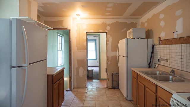 kitchen with light tile patterned floors, white appliances, a sink, light countertops, and backsplash