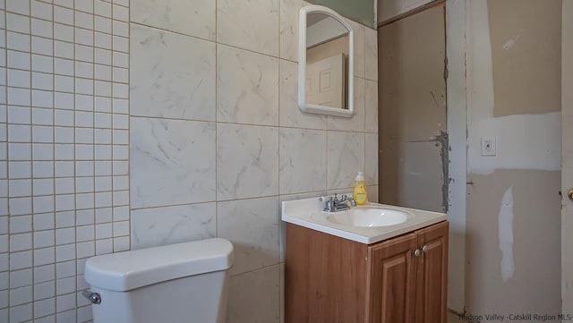 half bath with vanity, toilet, and tile walls