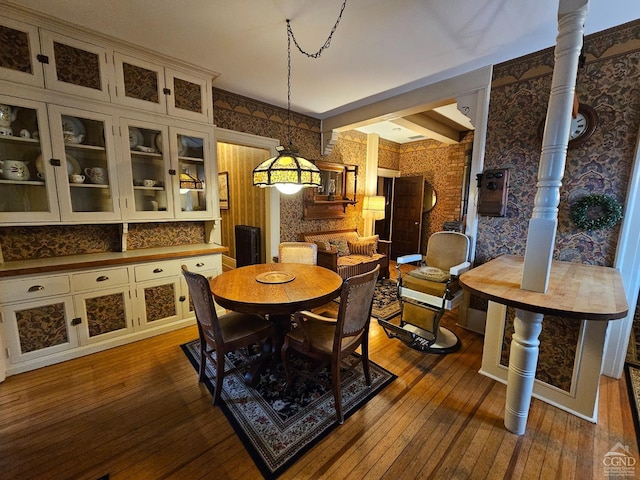 dining space featuring dark wood-type flooring, wallpapered walls, and beamed ceiling