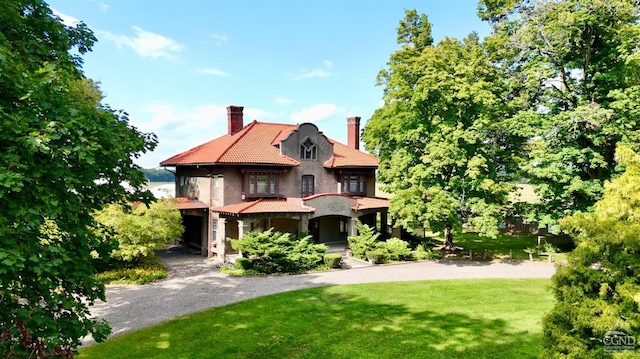view of front of home featuring a chimney, a front yard, stucco siding, a tiled roof, and gravel driveway