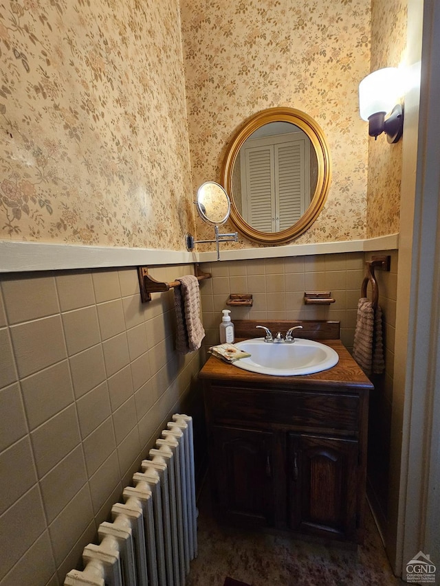 bathroom featuring wallpapered walls, radiator, wainscoting, vanity, and tile walls