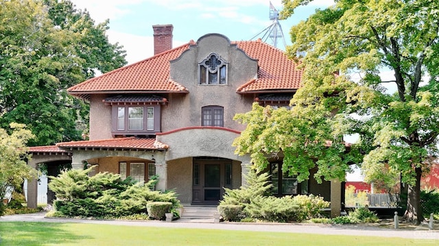 rear view of property with a tiled roof, a chimney, stucco siding, and covered porch