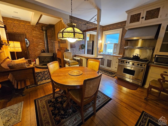 dining space featuring a wood stove, wood-type flooring, wallpapered walls, and beam ceiling
