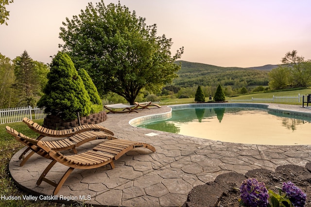 pool at dusk featuring a mountain view and a patio area