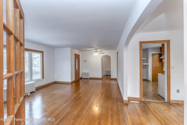 unfurnished living room with arched walkways, radiator heating unit, and wood finished floors