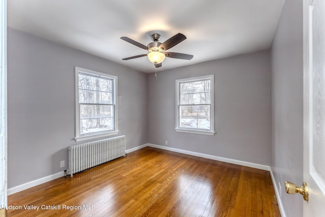 empty room with a wealth of natural light, baseboards, hardwood / wood-style floors, and radiator heating unit