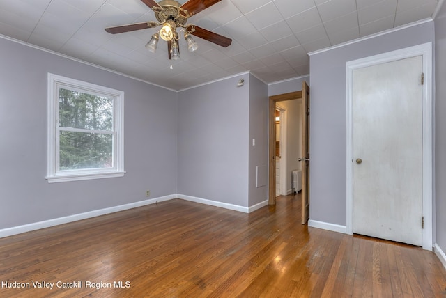 unfurnished room featuring a ceiling fan, baseboards, radiator, hardwood / wood-style floors, and crown molding