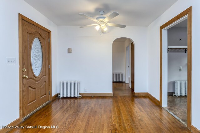 entrance foyer with radiator heating unit, arched walkways, and wood finished floors