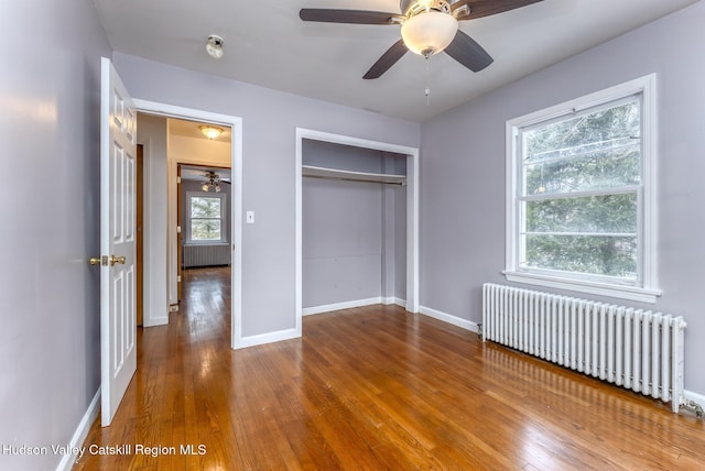 unfurnished bedroom with a closet, hardwood / wood-style floors, radiator heating unit, ceiling fan, and baseboards