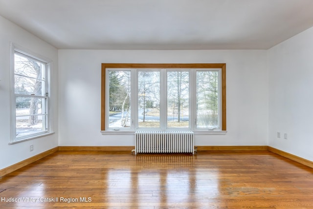 empty room with hardwood / wood-style flooring, radiator heating unit, and plenty of natural light