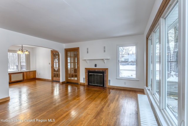 unfurnished living room featuring arched walkways, a healthy amount of sunlight, a brick fireplace, hardwood / wood-style floors, and radiator heating unit