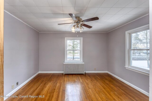 empty room featuring ceiling fan, hardwood / wood-style flooring, baseboards, ornamental molding, and radiator