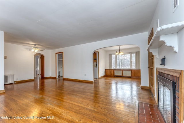 unfurnished living room featuring arched walkways, radiator, wood-type flooring, radiator heating unit, and a glass covered fireplace