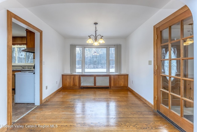 unfurnished dining area featuring radiator heating unit, wood finished floors, washer / dryer, and a notable chandelier