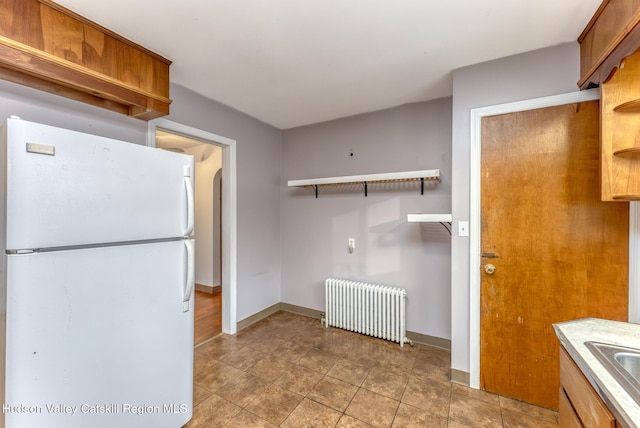 kitchen with a sink, freestanding refrigerator, brown cabinets, open shelves, and radiator heating unit