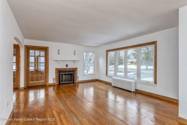 unfurnished living room featuring baseboards, arched walkways, radiator, wood finished floors, and a fireplace