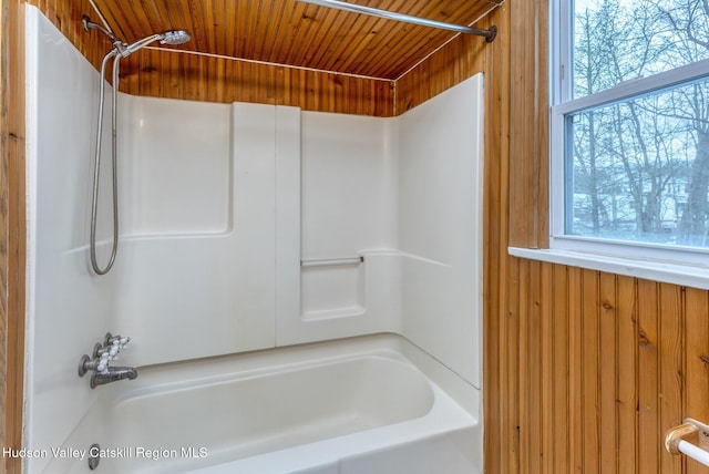 bathroom with wooden walls, bathtub / shower combination, and a healthy amount of sunlight