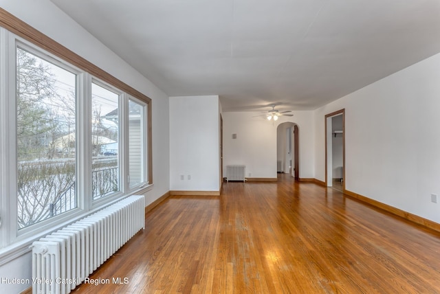 spare room with arched walkways, radiator heating unit, wood finished floors, and baseboards