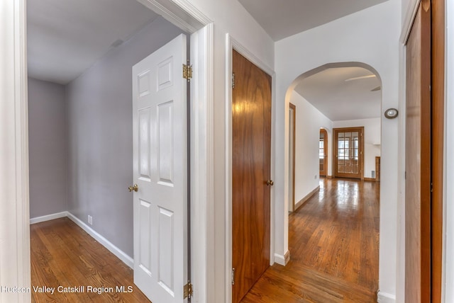 hall featuring baseboards, arched walkways, and wood finished floors