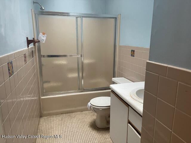 full bathroom featuring tile patterned flooring, bath / shower combo with glass door, and tile walls