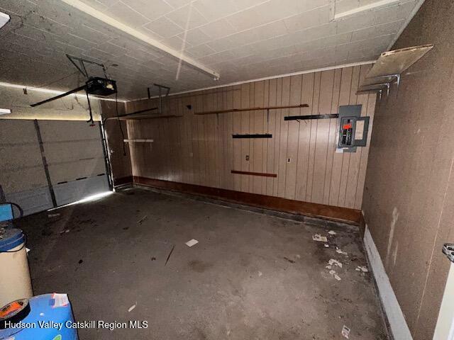 garage with baseboards, a garage door opener, wood walls, and electric panel