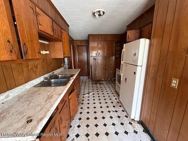 kitchen featuring white appliances, brown cabinetry, a sink, and light countertops
