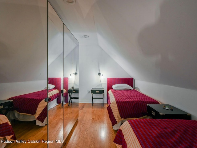 bedroom with hardwood / wood-style flooring, vaulted ceiling, and a closet