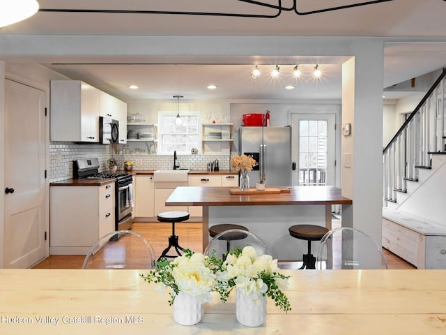 kitchen with wood counters, hanging light fixtures, white cabinetry, and stainless steel appliances