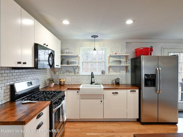 kitchen with sink, butcher block countertops, white cabinetry, hanging light fixtures, and stainless steel appliances