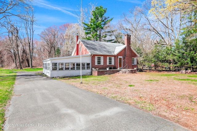 view of front facade featuring brick siding, a sunroom, a front lawn, and a chimney