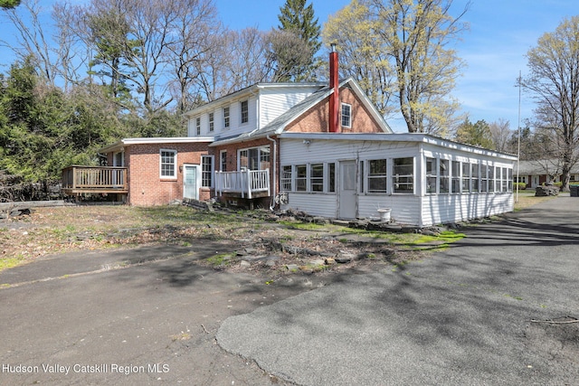 view of front facade featuring a chimney, a sunroom, brick siding, and a deck