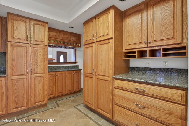 kitchen with open shelves, brown cabinetry, and dark stone counters
