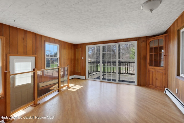 unfurnished room featuring a baseboard radiator, wooden walls, and light wood-style flooring