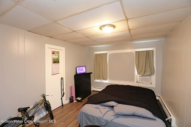 bedroom with a paneled ceiling, a baseboard heating unit, cooling unit, a baseboard radiator, and wood finished floors