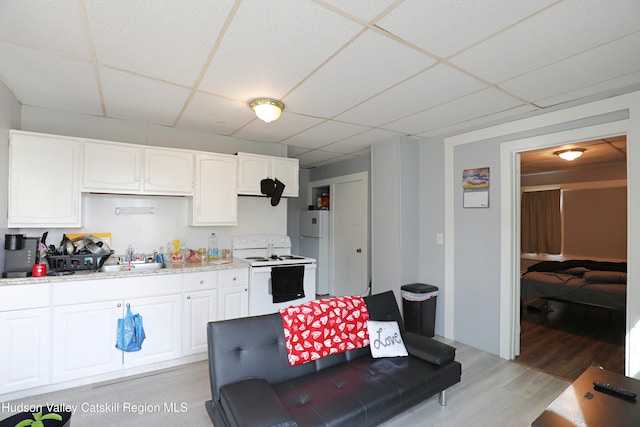 kitchen with light wood-type flooring, white appliances, light countertops, white cabinets, and a drop ceiling