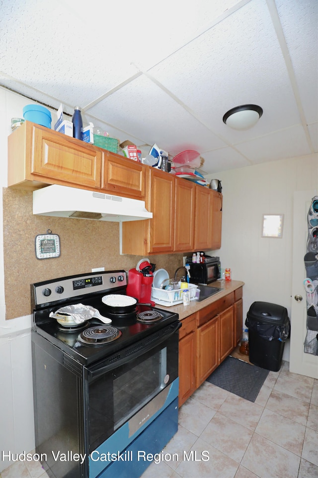 kitchen with light tile patterned floors, a drop ceiling, under cabinet range hood, a sink, and electric range oven
