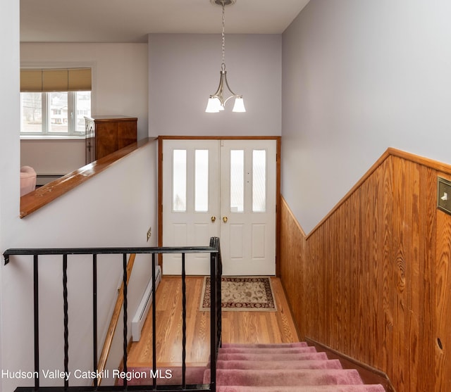 entryway featuring a chandelier, wood walls, light hardwood / wood-style floors, and a baseboard radiator