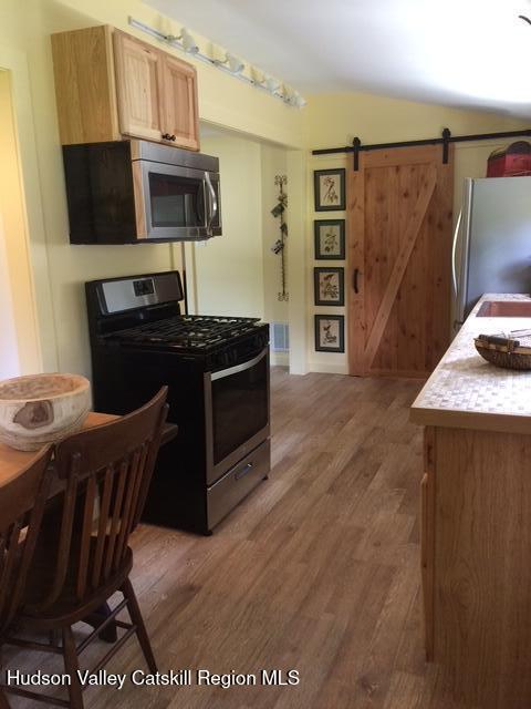 kitchen with lofted ceiling, light brown cabinetry, a barn door, appliances with stainless steel finishes, and wood finished floors
