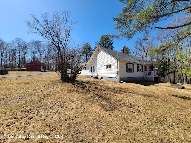 view of side of property with an outbuilding, roof with shingles, a porch, a garage, and a yard