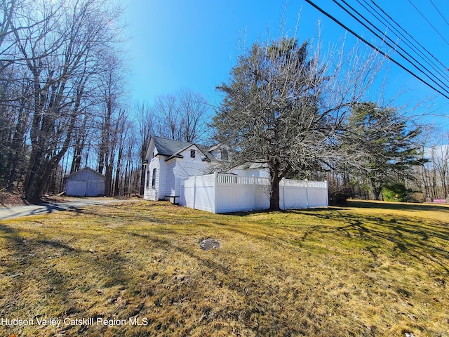 view of side of home featuring a lawn, an outbuilding, and fence