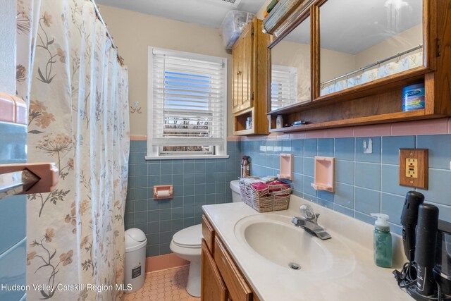 full bathroom featuring a wainscoted wall, tile patterned floors, toilet, vanity, and tile walls