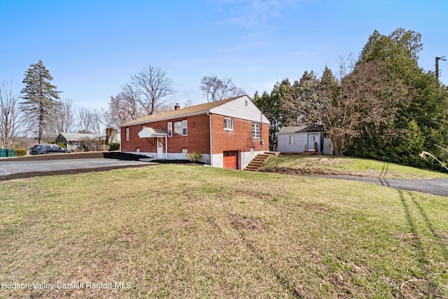 back of property featuring a chimney, brick siding, driveway, and a lawn