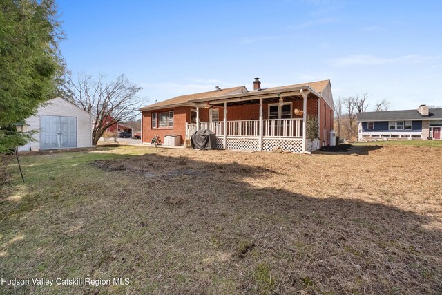 view of front of house with a chimney, a front yard, brick siding, an outbuilding, and a porch