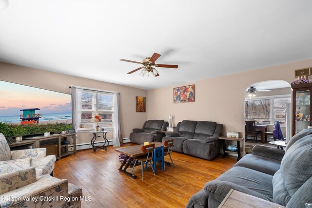 living area featuring a water view, baseboard heating, a ceiling fan, arched walkways, and wood-type flooring