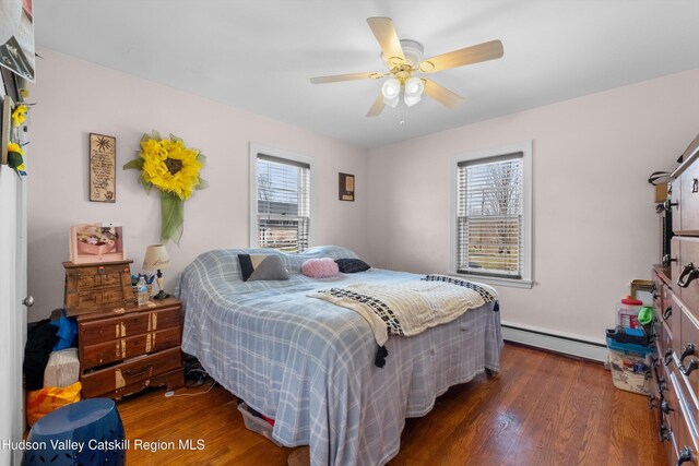 bedroom featuring a ceiling fan, wood finished floors, multiple windows, and baseboard heating