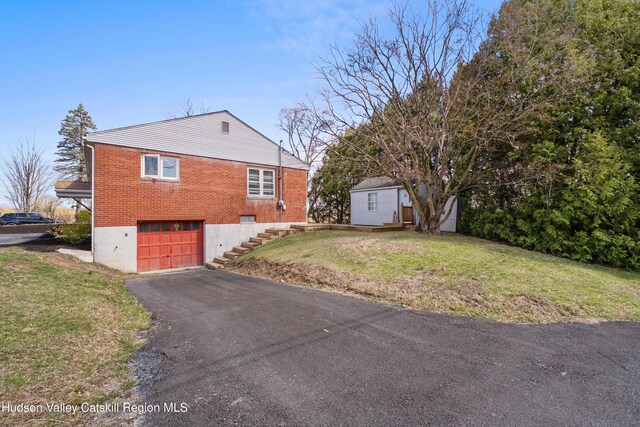 view of home's exterior featuring driveway, an outbuilding, brick siding, a lawn, and a garage
