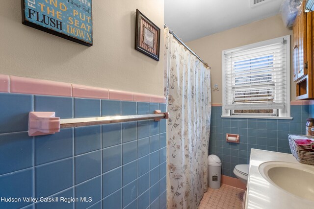 bathroom featuring tile patterned floors, a shower with shower curtain, toilet, wainscoting, and tile walls