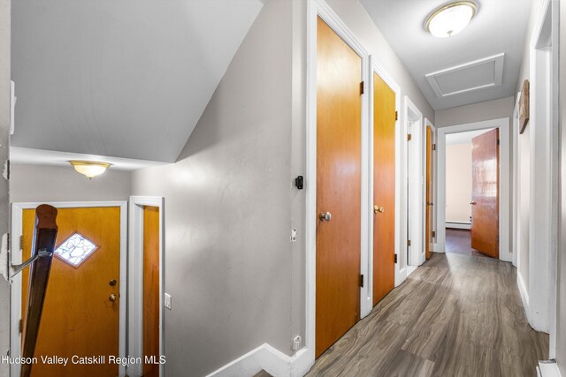 corridor with baseboards, baseboard heating, and wood finished floors